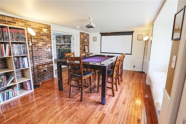 dining room with brick wall, light wood finished floors, a fireplace, and baseboards