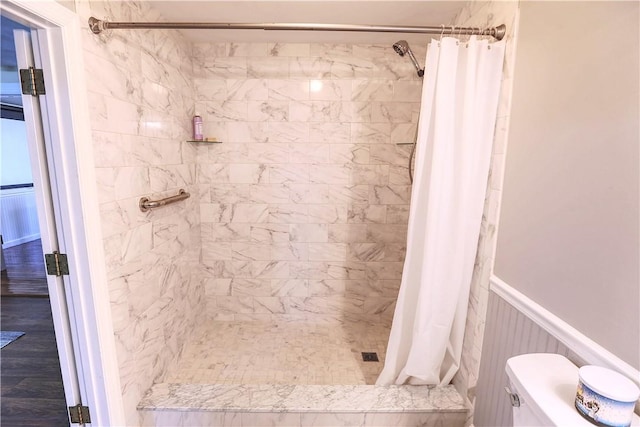 bathroom with toilet, a wainscoted wall, a shower stall, and wood finished floors