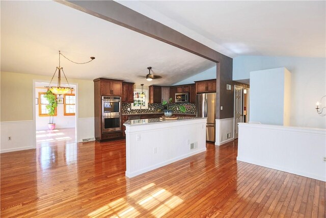 kitchen with lofted ceiling with beams, appliances with stainless steel finishes, light wood-style flooring, and a notable chandelier