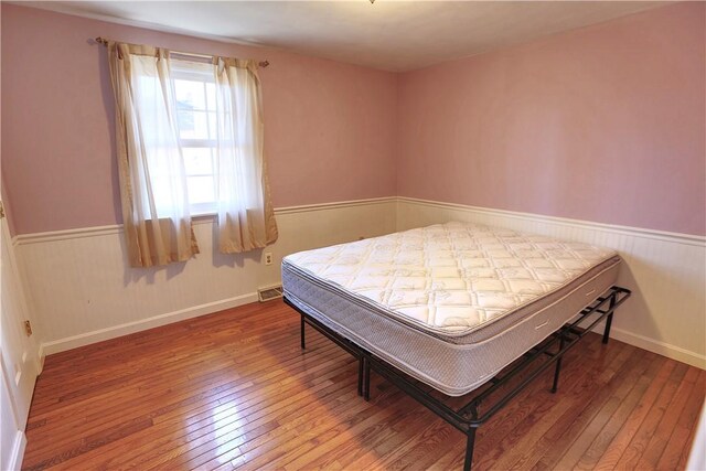 bedroom featuring wood-type flooring, visible vents, and wainscoting