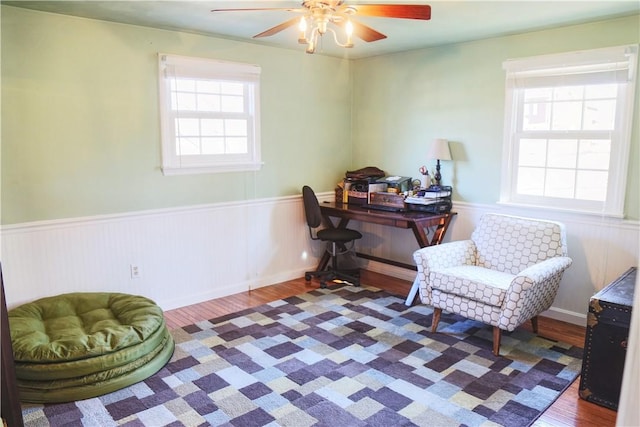 office area featuring a ceiling fan, a wainscoted wall, and wood finished floors