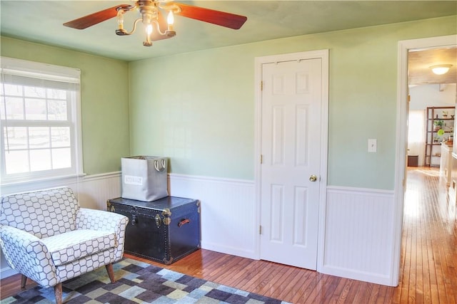 living area featuring a wainscoted wall, hardwood / wood-style floors, and a ceiling fan