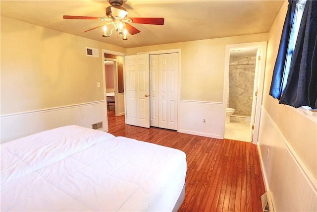 bedroom featuring wainscoting, visible vents, ensuite bath, and wood finished floors