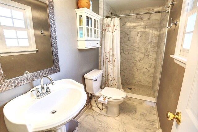bathroom with toilet, marble finish floor, a tile shower, and a sink
