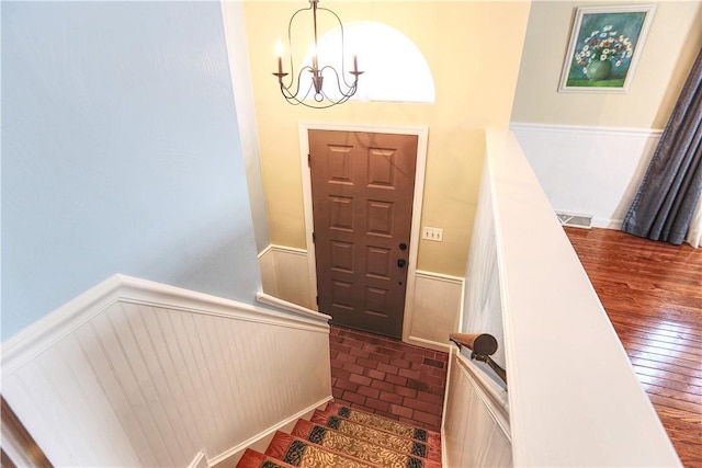 entrance foyer with brick floor, a wainscoted wall, visible vents, stairway, and an inviting chandelier