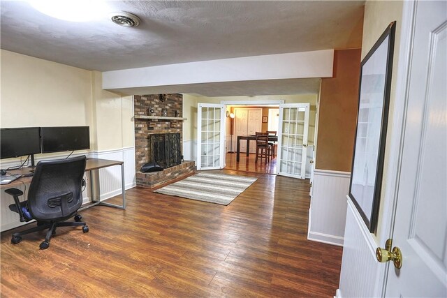 home office featuring a decorative wall, wood finished floors, visible vents, wainscoting, and a brick fireplace