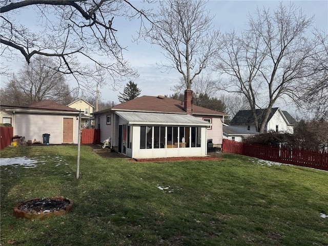 back of property with a fire pit, a yard, and a sunroom