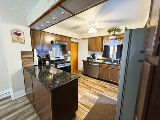 kitchen featuring sink, light hardwood / wood-style flooring, appliances with stainless steel finishes, dark stone countertops, and tasteful backsplash