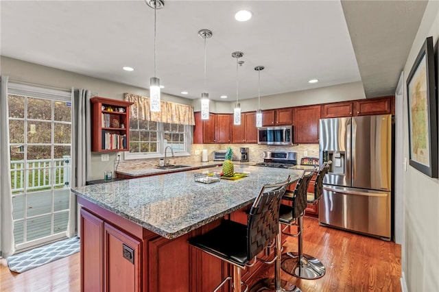 kitchen featuring appliances with stainless steel finishes, a kitchen breakfast bar, a kitchen island, pendant lighting, and light stone countertops