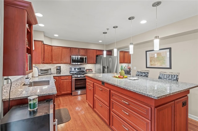 kitchen with appliances with stainless steel finishes, light stone counters, light hardwood / wood-style floors, a kitchen island, and decorative light fixtures