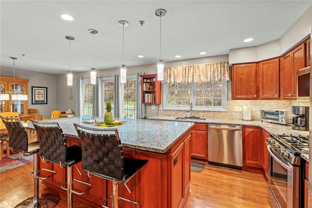 kitchen with sink, a breakfast bar area, light stone counters, hanging light fixtures, and stainless steel appliances