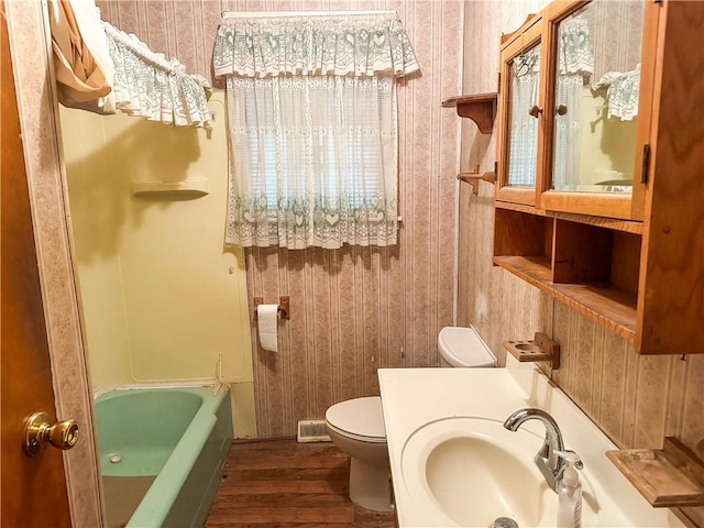 bathroom featuring wood-type flooring, toilet, sink, and a washtub