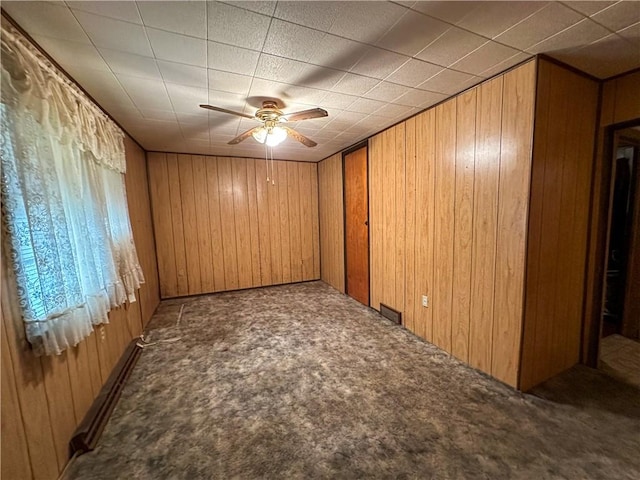 empty room with ceiling fan, wooden walls, carpet, and a baseboard heating unit