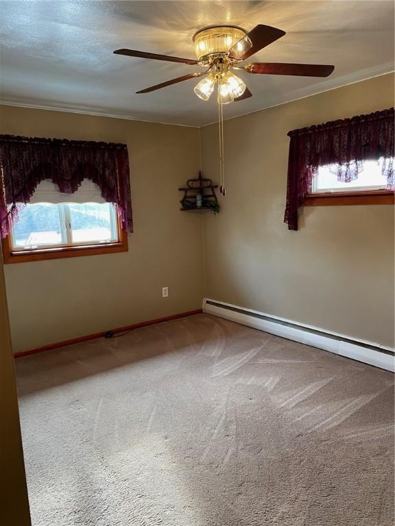 carpeted empty room featuring a baseboard heating unit, crown molding, and ceiling fan