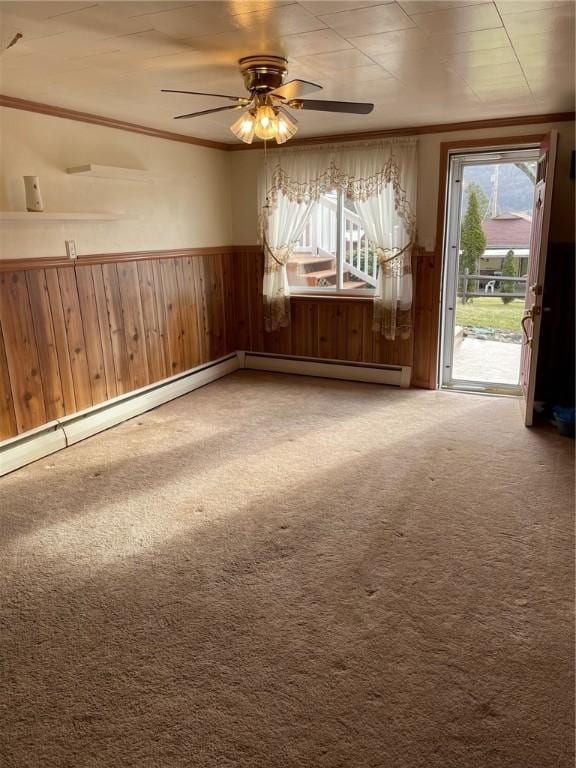 carpeted empty room with crown molding, ceiling fan, a baseboard radiator, and wood walls