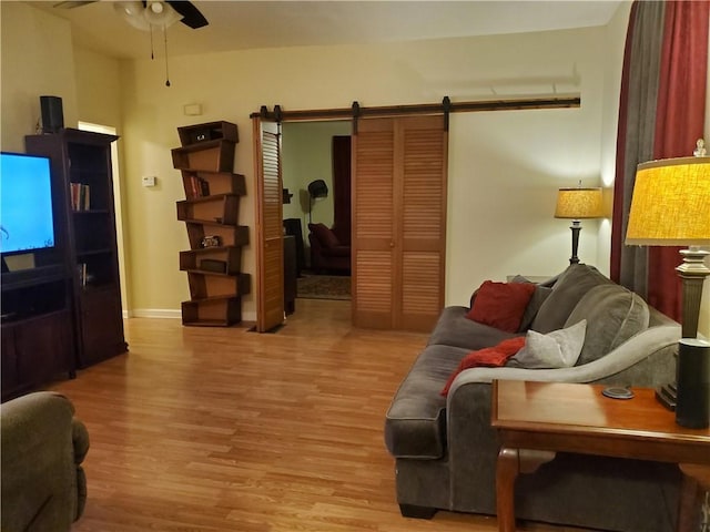 living room with a barn door, ceiling fan, and light wood-type flooring