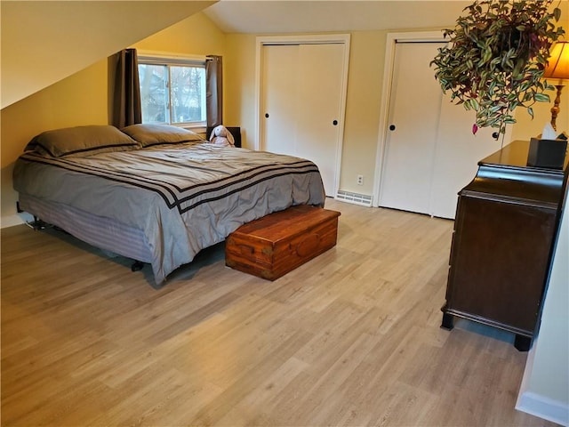 bedroom with lofted ceiling, light hardwood / wood-style flooring, and two closets