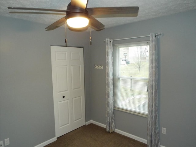 unfurnished room featuring dark colored carpet, ceiling fan, and a textured ceiling