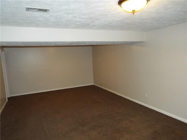 basement with a textured ceiling and dark colored carpet