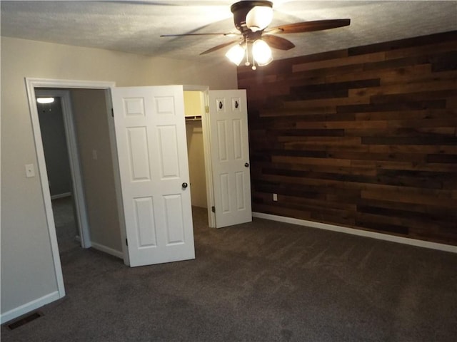 unfurnished bedroom with dark carpet, a textured ceiling, and wooden walls