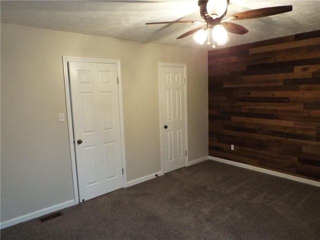 carpeted spare room with ceiling fan, a textured ceiling, and wood walls