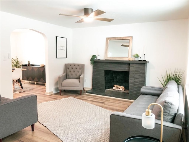 living room with wood-type flooring, ceiling fan, and a fireplace