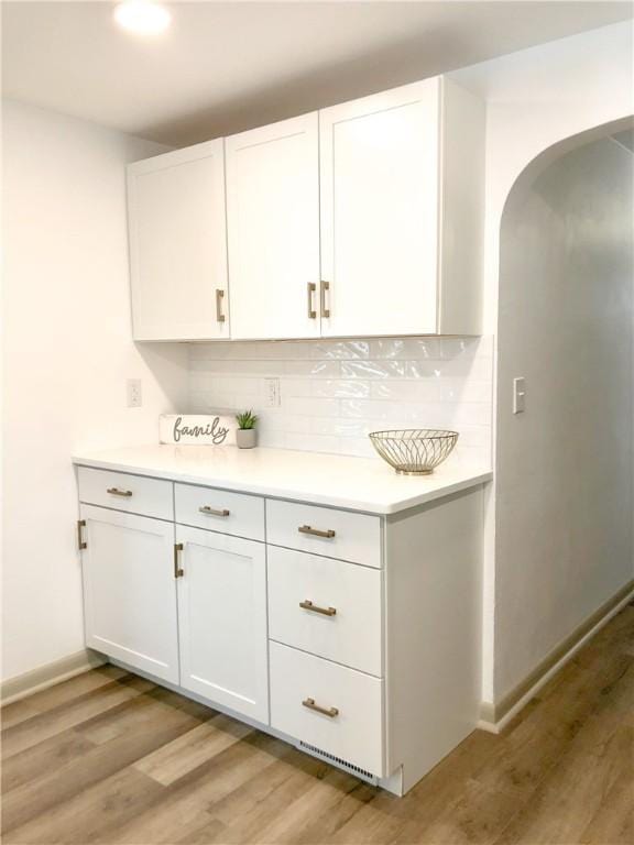 bar with tasteful backsplash, white cabinets, and light hardwood / wood-style floors