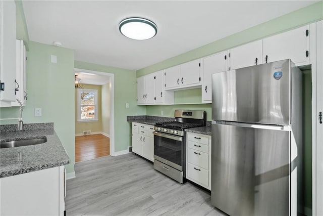 kitchen with light hardwood / wood-style flooring, stainless steel appliances, dark stone counters, and white cabinets