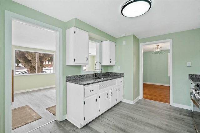 kitchen featuring white cabinetry, sink, dark stone countertops, light hardwood / wood-style floors, and stainless steel range oven