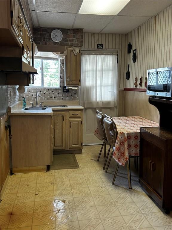 kitchen with tasteful backsplash, sink, a drop ceiling, and wood walls