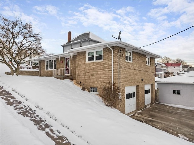 snow covered rear of property featuring a garage