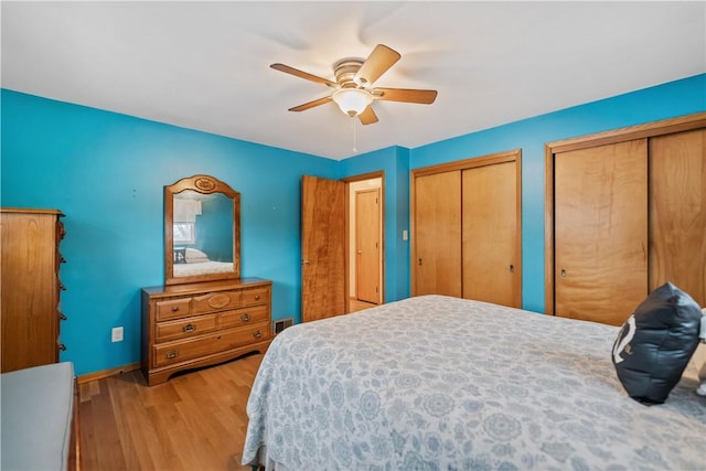 bedroom with two closets, light hardwood / wood-style floors, and ceiling fan