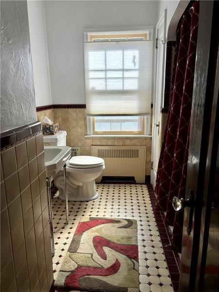 bathroom with tile walls, radiator heating unit, and toilet