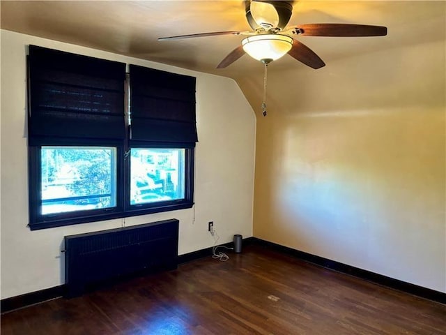 spare room with lofted ceiling, dark wood-type flooring, radiator heating unit, and ceiling fan