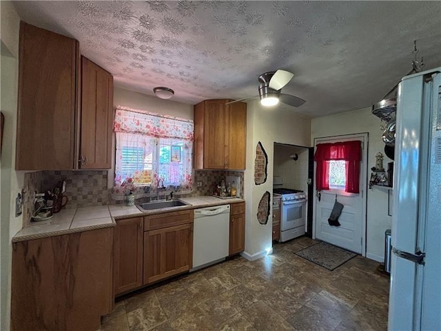 kitchen with sink, white appliances, ceiling fan, tasteful backsplash, and a textured ceiling