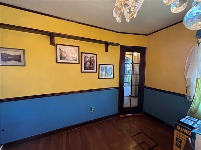 spare room featuring dark wood-type flooring, ornamental molding, and a notable chandelier