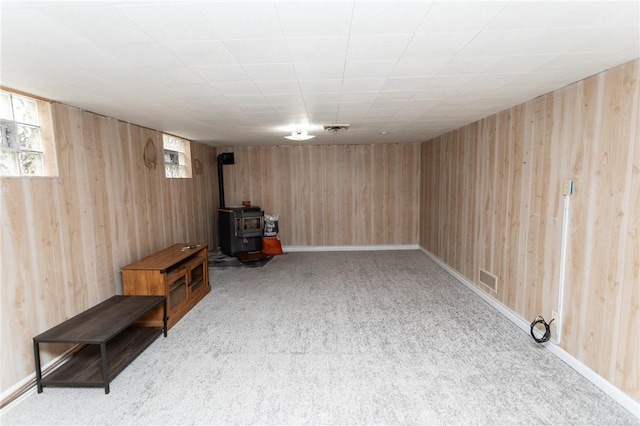 basement featuring light carpet, wood walls, and a wood stove