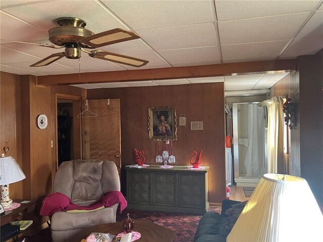 living room with a paneled ceiling, ceiling fan, and wood walls