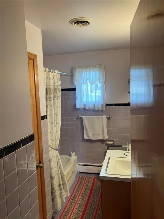 bathroom featuring vanity, a baseboard heating unit, tile walls, and shower / bathtub combination with curtain