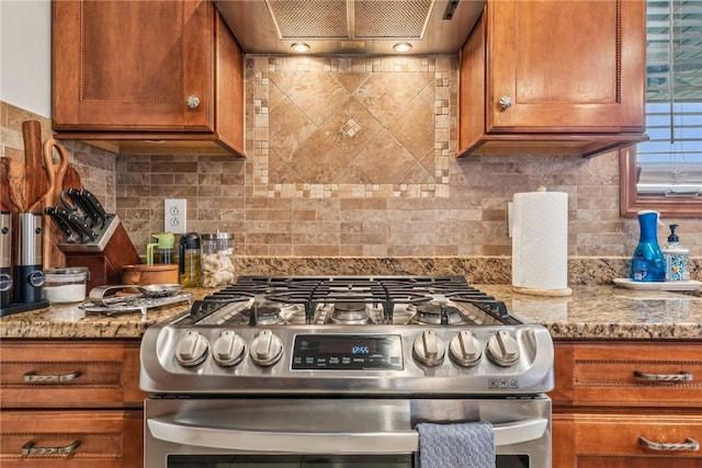 kitchen featuring wall chimney range hood, gas range, light stone countertops, and backsplash