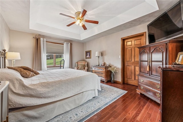 bedroom with dark wood-type flooring, ceiling fan, and a tray ceiling