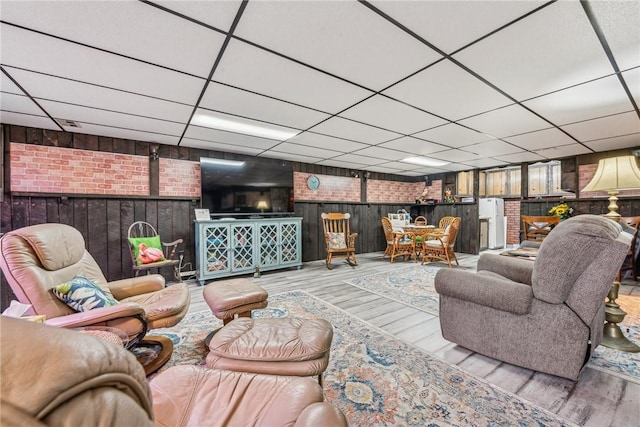 living room with brick wall, hardwood / wood-style floors, and a drop ceiling