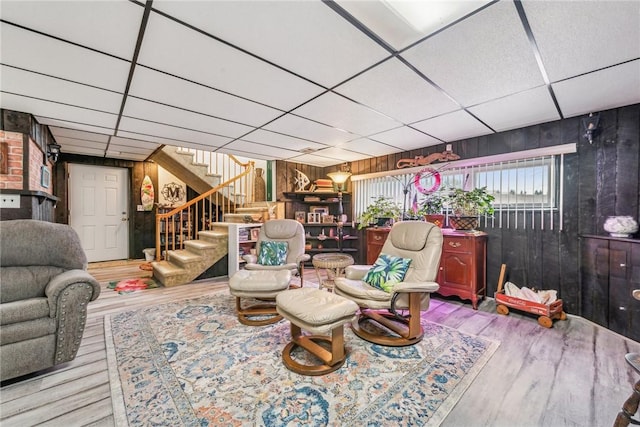 living area with a drop ceiling, hardwood / wood-style floors, and wooden walls