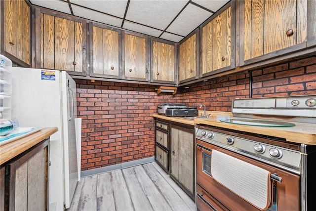 kitchen with stove, light hardwood / wood-style floors, brick wall, a drop ceiling, and white fridge