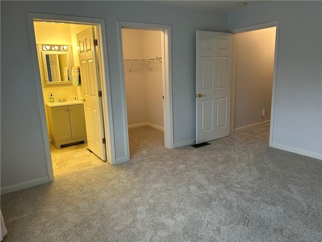 unfurnished bedroom with ensuite bathroom, sink, a walk in closet, light carpet, and a closet