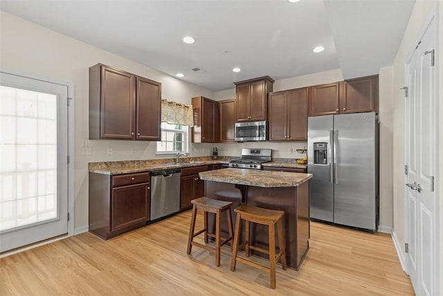 kitchen featuring a breakfast bar, a center island, dark stone countertops, light wood-type flooring, and appliances with stainless steel finishes