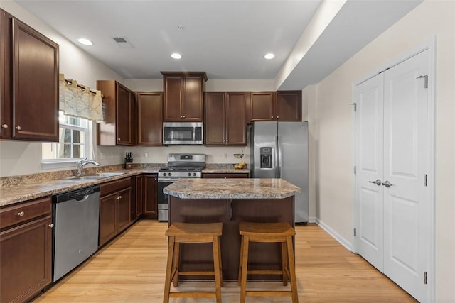 kitchen featuring sink, a center island, appliances with stainless steel finishes, a kitchen breakfast bar, and light hardwood / wood-style floors