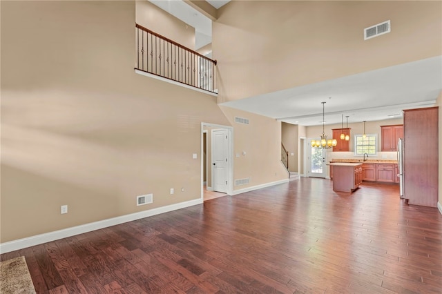 unfurnished living room featuring dark wood-type flooring, sink, a chandelier, and a towering ceiling