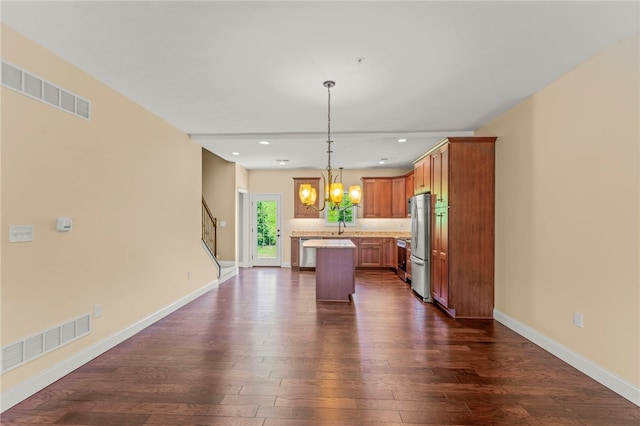 kitchen with stainless steel fridge, hanging light fixtures, a center island, a notable chandelier, and dark hardwood / wood-style flooring