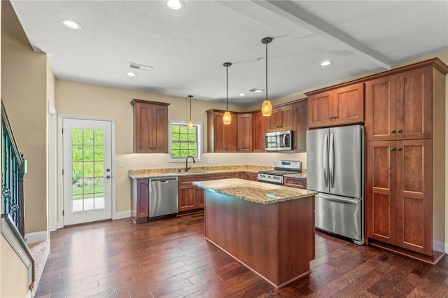 kitchen with hanging light fixtures, dark hardwood / wood-style floors, a kitchen island, stainless steel appliances, and light stone countertops